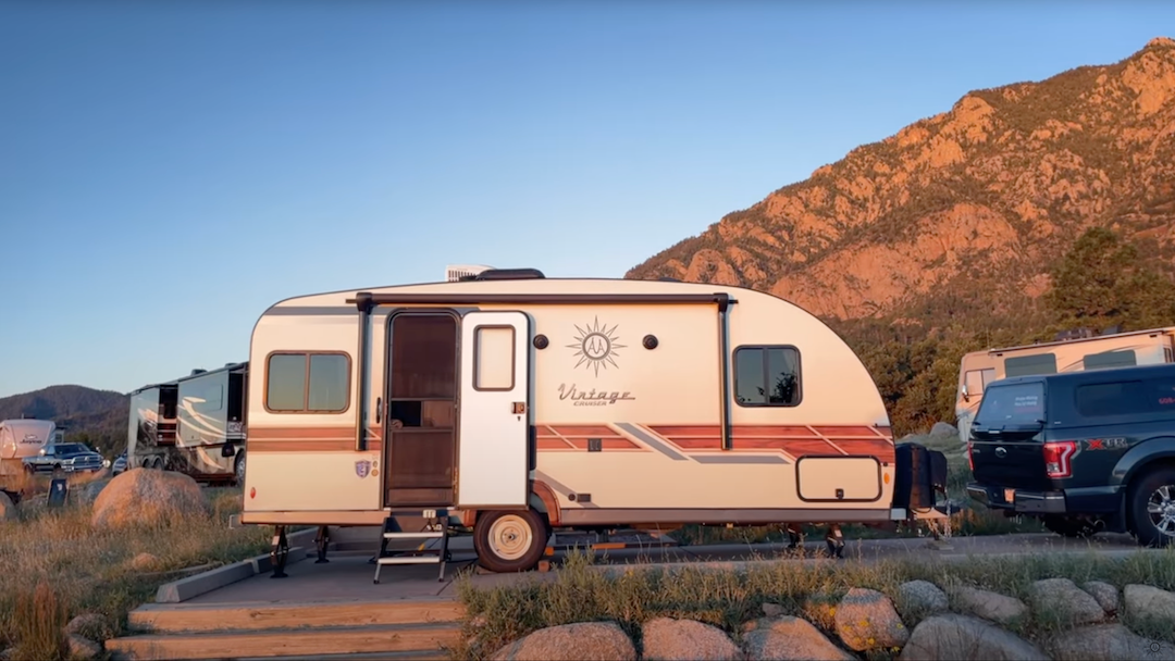 a small travel trailer parked by a mountain in the sunrise